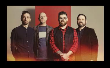 Four men stand looking straight at the camera