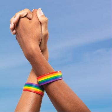 Two hands intertwined, with rainbow bracelets