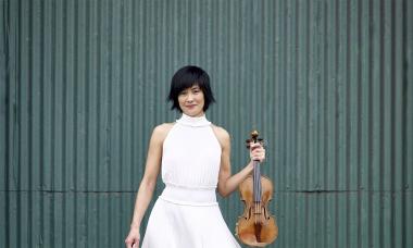 Jennifer Koh in a white dress, holding her violin