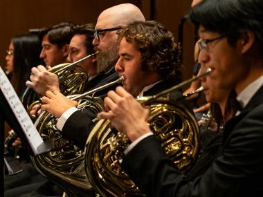 A closeup of four brass French horn players of the UC Davis Symphony Orchestra in concert black attire (Phil Daley/UC Davis)