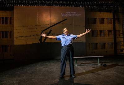 A woman in a police costume stands on stage with her hands extended. 