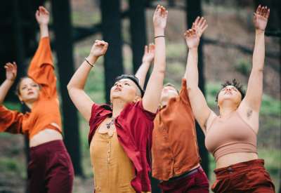 Photo of four dancers wearing red and orange clothes with their hands raised in the air